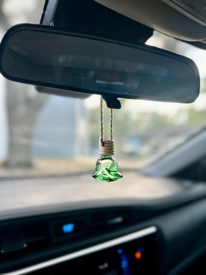 Pode incluir: Um aromatizador de carro de vidro verde em forma de rosa pendurado no espelho retrovisor de um carro.