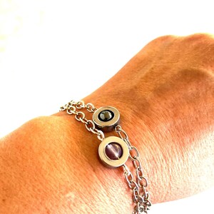 May include: A silver bracelet with two circular charms, each containing a dark stone. The bracelet has a double chain design. The charms are set in a silver bezel.