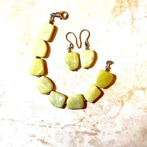Peut inclure: Un ensemble de bijoux comprenant un bracelet et des boucles d'oreilles. Le bracelet et les boucles d'oreilles sont faits de pierres jaune-vert clair de forme irrégulière. Le bracelet a un fermoir argenté. Les boucles d'oreilles ont des crochets argentés.