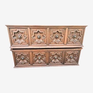 May include: A two-piece wooden dresser with eight drawers. Each drawer is square and features a carved starburst design with a central knob. The wood has a warm, medium brown tone, and the piece has a vintage aesthetic.