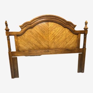 May include: A wooden headboard with a light brown finish. The headboard features a curved top with decorative moulding and a chevron pattern on the main panel. The design includes two vertical posts with finials.