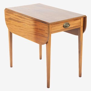 May include: A light brown, wooden drop-leaf table with a single drawer and brass hardware. The table has four slender legs and a rectangular top that can be folded down. The table is approximately 30 inches long.