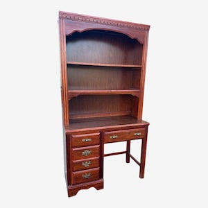 May include: A dark brown wooden desk with a hutch. The desk has four drawers on the left and two drawers on the right, with brass-colored hardware. The hutch has three shelves and an arched top. The desk is made of wood.