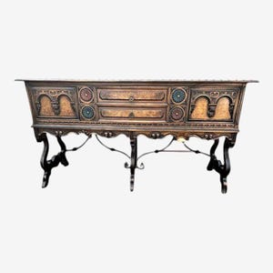 May include: A dark brown antique console table with two drawers and decorative floral accents. The table has ornate carvings and is supported by black, curved legs and a wrought iron base. The table is approximately 72 inches long.