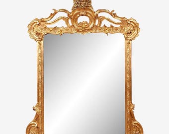 May include: A rectangular gold-colored mirror with an ornate, baroque-style frame. The frame features intricate carvings, including floral and scrollwork designs. The top of the mirror has a decorative crest, and the overall design is symmetrical.
