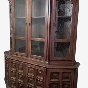 May include: A large, dark brown wooden cabinet with glass-fronted doors and decorative carved panels. The cabinet has a curved top and multiple storage compartments, including glass shelves and a lattice-patterned door.