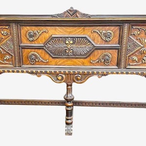 May include: A large, antique wooden sideboard with ornate carvings and brass accents. The dark brown cabinet features detailed floral and geometric designs, supported by decorative legs. The piece has a classic, vintage aesthetic.
