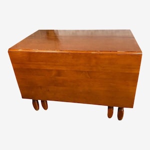 May include: A wooden drop-leaf table with a warm, medium-brown finish. The table has a rectangular shape with rounded legs. The top surface appears glossy. The table is a versatile piece of furniture.