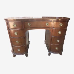 Könnte beinhalten: Ein Holzschreibtisch mit geschwungenem Design und brauner Oberfläche. Der Schreibtisch hat mehrere Schubladen mit Messingbeschlägen und eine geschwungene Front. Der Schreibtisch hat einen klassischen, eleganten Stil, geeignet für ein Homeoffice oder Arbeitszimmer.