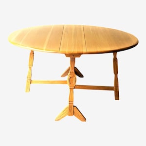 May include: A light brown, oval-shaped wooden table with a pedestal base. The tabletop is made of several wooden planks. The table has four legs and a central support structure. The table is approximately 48 inches in diameter.