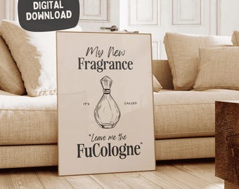 May include: A framed print with the text "My New Fragrance" and a drawing of a perfume bottle. Below the bottle, the text reads "Leave me the FuCologne". The print is leaning against a beige sofa.
