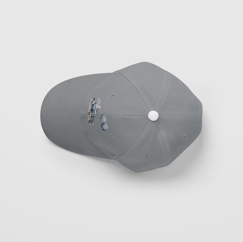 Op de afbeelding: Een grijze baseballpet met een witte knoop bovenop. De pet heeft een kleine, kleurrijke afbeelding van een auto met een blauw en wit ontwerp op de voorkant.