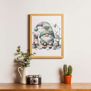 May include: A framed illustration of a gnome wearing a green hat with a floral embellishment. The gnome is holding a spool of thread and surrounded by sewing supplies.
