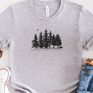 May include: A grey t-shirt with a black silhouette of a forest and the text "Appalachian Trail".