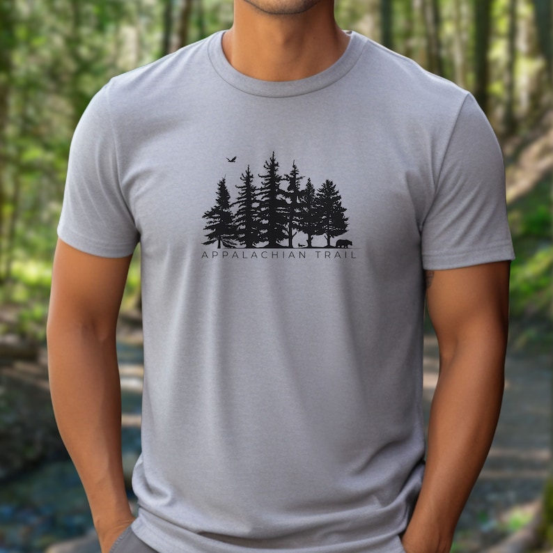 May include: A grey t-shirt featuring a black silhouette of a forest with a bird flying overhead and the text "Appalachian Trail".