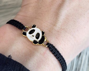 Op de afbeelding: Zwart gevlochten armband met een pandabeer bedel. De bedel heeft zwart-witte emaille en goudkleurige accenten. De armband wordt om een pols gedragen.