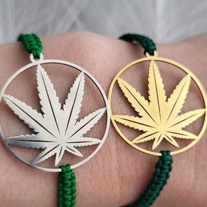 Peut inclure: Deux bracelets avec un motif de feuille de cannabis. L'un est de couleur argentée, l'autre dorée. Les deux ont un cordon vert tressé et une fermeture à nœud coulissant.