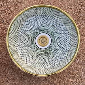 Peut inclure: Un lavabo rond décoratif avec un motif géométrique blanc et vert. Le lavabo a un bord doré et un drain doré. Le lavabo est conçu pour une salle de bain ou une cuisine.