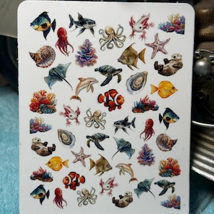 Op de afbeelding: Een witte stickerpagina met diverse aquarel illustraties van zeeleven. De ontwerpen omvatten vissen, octopussen, zeeschildpadden, zeesterren en koraal. De stickerpagina heeft afgeronde hoeken.