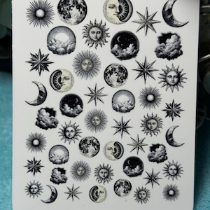 Puede incluir: Una hoja de pegatinas rectangular blanca con ilustraciones celestiales. El diseño incluye soles, lunas, estrellas y nubes en blanco y negro. La hoja de pegatinas tiene esquinas redondeadas.
