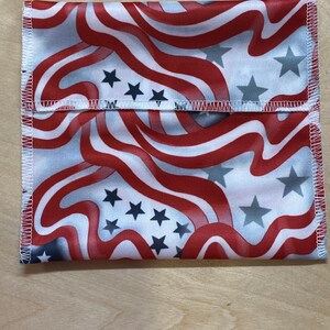 Puede incluir: Un artículo de tela plegada con un diseño patriótico. Presenta rayas onduladas rojas y blancas y estrellas azules dispersas. Los bordes están acabados con costuras blancas, creando un accesorio decorativo y funcional.
