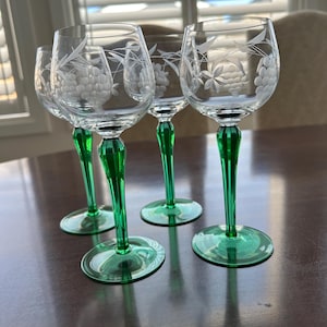 Op de afbeelding: Set van vier heldere glazen wijnglazen met gegraveerde druivenmotieven en groene stelen.