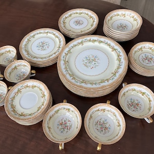 Puede incluir: Un juego completo de vajilla de porcelana vintage. El juego incluye platos, cuencos, platillos y tazas de té. Cada pieza presenta un fondo color crema con un centro floral y un borde dorado y verde. Las tazas de té tienen asas doradas.