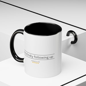 May include: White ceramic mug with a black interior, handle, and rim. The mug features the text "Re: Kindly following up" and "AGENT'S LIFE" with five gold stars.