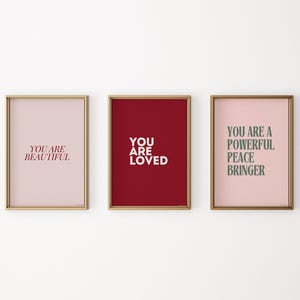 May include: Three framed prints with motivational messages. The first print has a pink background and says "You are beautiful" in red text. The second print has a red background and says "You are loved" in white text. The third print has a pink background and says "You are a powerful peace bringer" in green text.