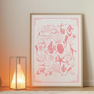 Könnte beinhalten: Ein rosa-weißer gerahmter Druck mit einem Design aus verschiedenen Muscheln, Seepferdchen und Seesternen. Der Druck ist auf weißem Hintergrund und hat einen rosa Rand.