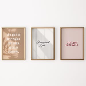 May include: Three framed prints with inspirational quotes. The first print has a beige background with the text "You are not responsible for other peoples emotions". The second print has a white background with the text "I am proud of you". The third print has a light pink background with the text "You are beautiful".