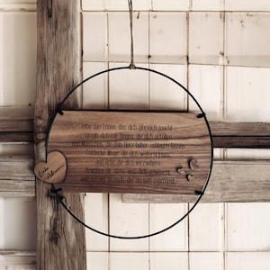 Könnte beinhalten: Holzschild mit herzförmigem Akzent und schwarzem Metallring. Das Schild zeigt gravierten Text auf Deutsch und ein kleines Herz mit dem Namen "Adrienne". Das Schild wird von einer natürlichen Schnur gehalten.