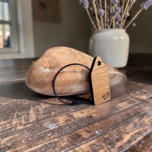 May include: A light brown wooden tag with a dark brown envelope icon engraved on the bottom right corner. The tag features a circular hole at the top and is attached to a thin, flexible black circular wire loop with a small metal fastener.