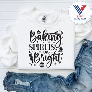 Könnte beinhalten: Weißer Pullover mit schwarzem Text, der "Baking Spirits Bright" lautet, mit einem Lebkuchenmann, einem Nudelholz, einem Schneebesen, einem Donut, einem Herzen und Schneeflocken.