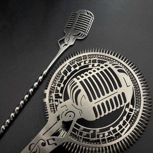 Peut inclure: Une passoire à cocktail en argent avec un motif de microphone et des notes de musique. La passoire a une longue poignée avec un design torsadé. La poignée est attachée à une passoire ronde et plate avec un motif de microphone au centre. Le motif du microphone est entouré de notes de musique.