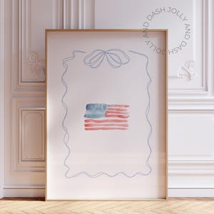 Könnte beinhalten: Aquarelldruck der amerikanischen Flagge in einem Holzrahmen. Die Flagge zeigt rote und weiße Streifen und ein blaues Feld mit Sternen. Das Kunstwerk ist von einer blauen Strichzeichnung umgeben und der Text "AND DASH JOLLY" in einem Kreis.