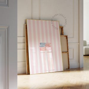 Peut inclure: Une œuvre d'art encadrée avec un fond à rayures roses et blanches et un drapeau américain à l'aquarelle au centre. L'œuvre est appuyée contre un mur, avec le texte "JOLLY AND DASH" en cercle en haut.