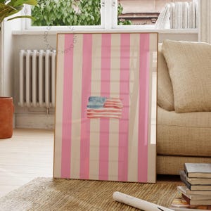 Könnte beinhalten: Gerahmtes Kunstwerk mit einem Aquarell-Design der amerikanischen Flagge. Das Kunstwerk hat einen rosa-weiß gestreiften Hintergrund. Die Flagge ist in Blau und Rot gemalt. Der Rahmen ist goldfarben.