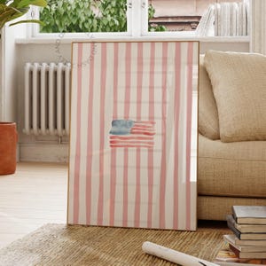 Könnte beinhalten: Gerahmtes Aquarellbild mit einer stilisierten amerikanischen Flagge. Der goldfarbene Rahmen umgibt ein Muster aus vertikalen rosa und weißen Streifen. Die Flagge ist in Blau- und Rottönen gemalt.
