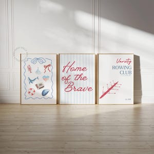 Op de afbeelding: Drie ingelijste kunstdrukken met nautische en patriottische thema's. Eén print toont aquarel illustraties van een kreeft, een walvis en een schelp. De tweede print zegt "Home of the Brave" op een blauw gestreepte achtergrond. De derde print zegt "Varsity Rowing Club".