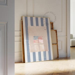 Könnte beinhalten: Gerahmtes Kunstwerk mit hellblau-weiß gestreiftem Hintergrund und einem Briefmarken-Design. Die Briefmarke zeigt eine Aquarell-amerikanische Flagge. Das Kunstwerk wird zusammen mit anderen gerahmten Stücken an einer weißen Wand präsentiert.