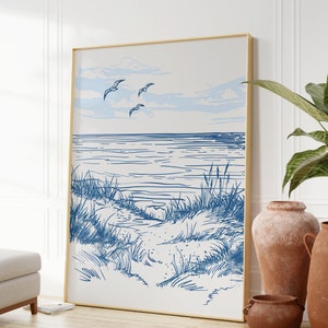 Peut inclure: Un dessin au trait bleu et blanc d'une scène de plage avec des mouettes volant au-dessus. Le dessin est encadré dans un cadre doré et accroché à un mur blanc.