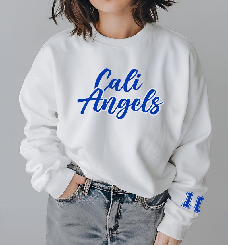 Puede incluir: Sudadera blanca de cuello redondo con las palabras "Cali Angels" en escritura azul en el pecho. El n&uacute;mero "10" est&aacute; impreso en azul en la manga derecha. La persona lleva vaqueros azules.