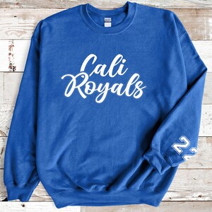 Puede incluir: Una sudadera azul real con la inscripci&oacute;n blanca "Cali Royals" en escritura cursiva en el pecho. El n&uacute;mero "22" est&aacute; impreso en blanco en la manga izquierda. La sudadera es de material suave.