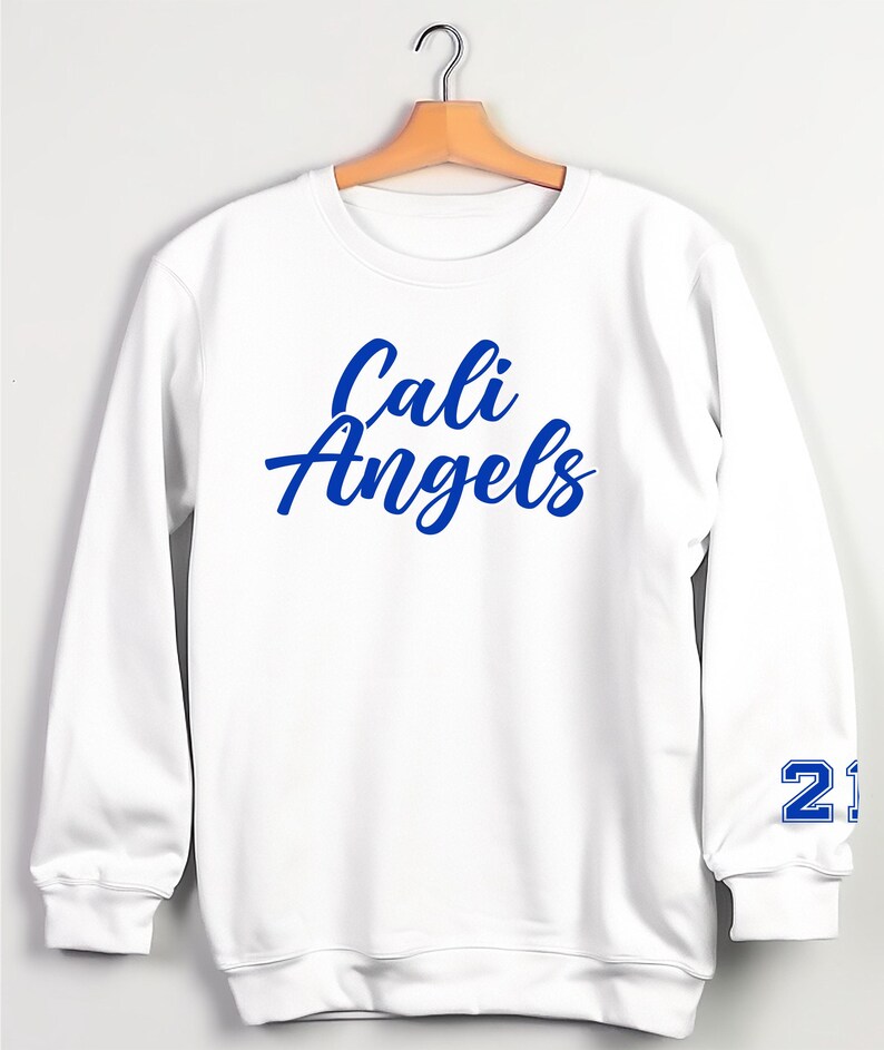 Puede incluir: Sudadera blanca con las palabras "Cali Angels" en escritura azul en el pecho. El n&uacute;mero "21" est&aacute; impreso en azul en la manga izquierda. La sudadera est&aacute; colgada en una percha de madera.