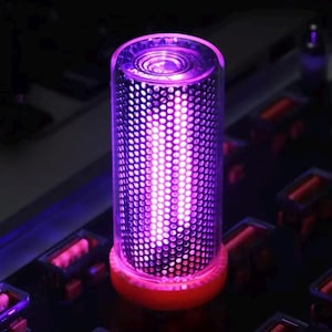 May include: A cylindrical light fixture featuring a perforated metal mesh sleeve that emits a vibrant purple glow. The light is encased in a clear outer shell and is mounted on a circular orange base, creating a focused and intense illumination.