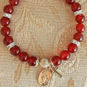 Op de afbeelding: Rode edelsteen armband met gouden accenten en een gouden bedel met de Maagd Maria en een kruis.