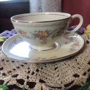 May include: A vintage teacup and saucer set with a floral pattern in shades of yellow, pink, and green. The set has a gold trim around the edges.
