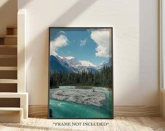 May include: A framed photograph of a mountain range with a river flowing through a valley. The sky is blue with white clouds. The mountains are covered in snow and trees.