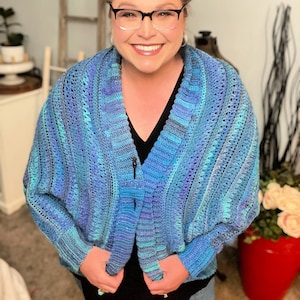 May include: A blue and purple crocheted cardigan with a loose fit and a V-neck. The cardigan is made with a textured stitch and has a striped pattern.